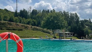 A swimming pool with a lifebuoy, a diving platform, and a gazebo in the background. - Modern vacation apartment for two (Klingenthal)
