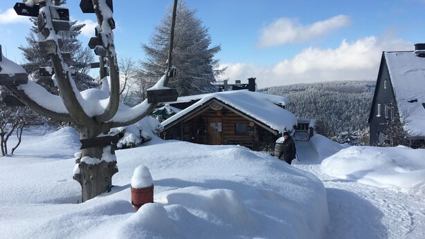 A snow-covered cabin with a wooden exterior, surrounded by snow-covered trees and a clear sky. - Modern vacation apartment for two (Klingenthal)