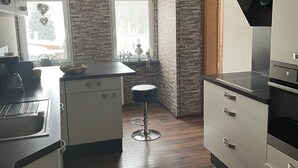 A compact kitchen with a central island, white cabinetry, a built-in oven, and a stone accent wall. - Modern vacation apartment for two (Klingenthal)