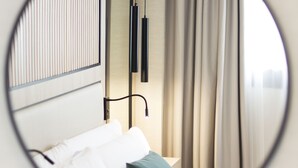 A circular view of a hotel room with a bed, pillows, a nightstand, and curtains.