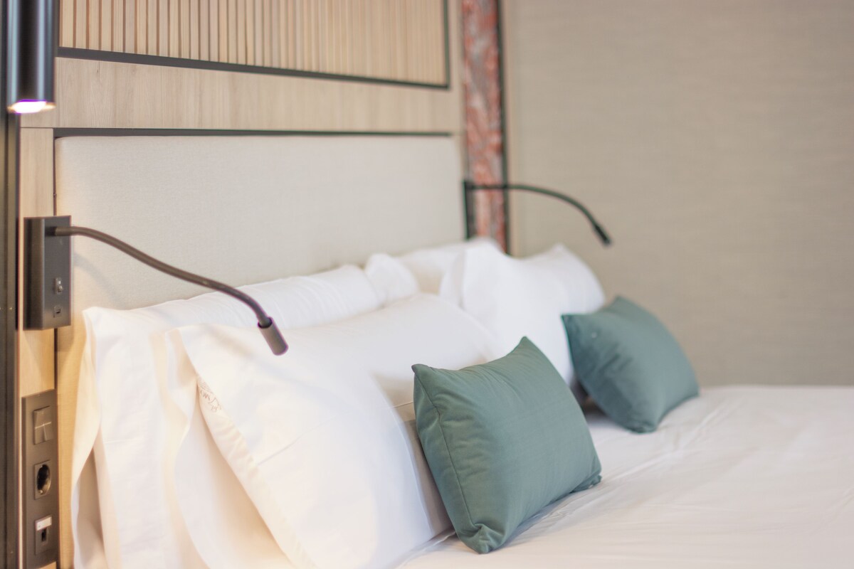 Una cama bien tendida con sábanas blancas y dos almohadas verdes.