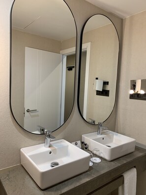 Une salle de bain avec deux lavabos blancs, un grand miroir et une porte donnant sur une autre pièce.