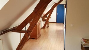 A spacious attic room with a wooden staircase, wooden flooring, and a blue door in the background.