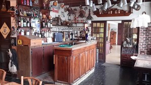 A bar area with wooden cabinets, shelves with bottles, and hanging lights.