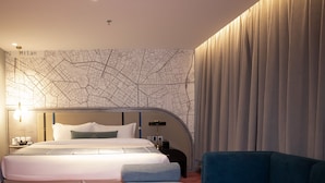 Habitación de hotel con cama, sofá azul, una mesita y un mural de mapa.