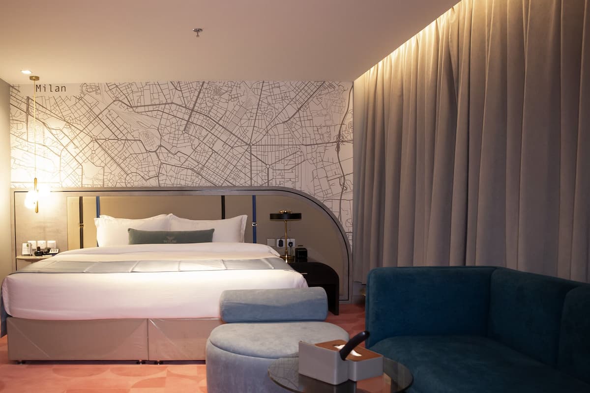 A hotel room with a bed, a blue sofa, a small table, and a map wall.