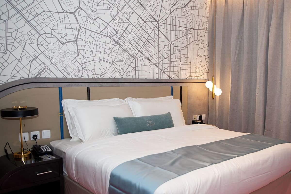 A hotel room with a large bed, a map on the wall, a bedside table with a lamp, and a curtain.