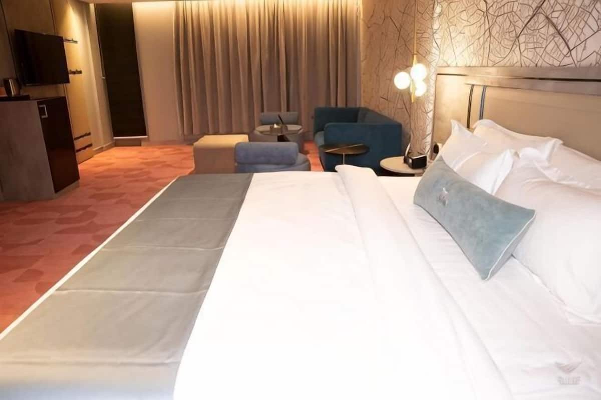 A hotel room with a large bed, a seating area with a chair and ottoman, a small table, and a television.