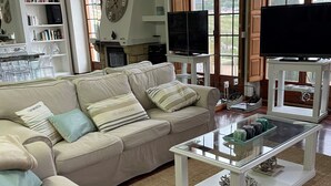 A living room with a beige sofa, a glass coffee table, and a television on a stand. - Chalet DE Lujo (Somo)