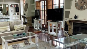 A spacious living room with a glass dining table, a fireplace, a large clock, and a television. - Chalet DE Lujo (Somo)