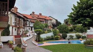 A courtyard with a swimming pool, potted plants, and a building with a tiled roof. - Chalet DE Lujo (Somo)
