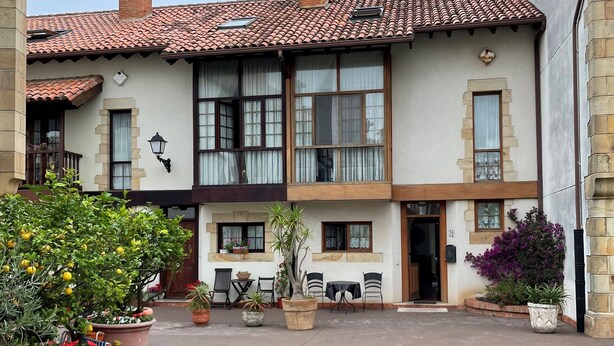 A two-story building with a courtyard, featuring a tiled roof, large windows, and potted plants. - Chalet DE Lujo (Somo)
