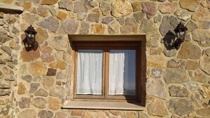Paret de pedra amb una finestra que presenta un marc de fusta i cortines blanques.