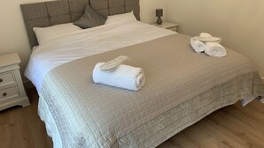 A neatly made bed with a grey headboard, white linens, and rolled towels on the side. - Vale View - Sleeps 6 - Pets Ok - Garden - Parking (Melton Mowbray)