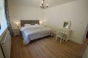 A bedroom with a bed, bedside tables, a nightstand, a chair, a dresser, a mirror, and a chandelier. - Vale View - Sleeps 6 - Pets Ok - Garden - Parking (Melton Mowbray)