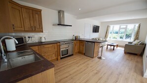 A modern kitchen with wooden cabinets, stainless steel appliances, and a large window providing natural light. - Vale View - Sleeps 6 - Pets Ok - Garden - Parking (Melton Mowbray)