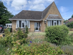 A two-story house with a pitched roof, a front porch, and a garden with various plants and flowers.