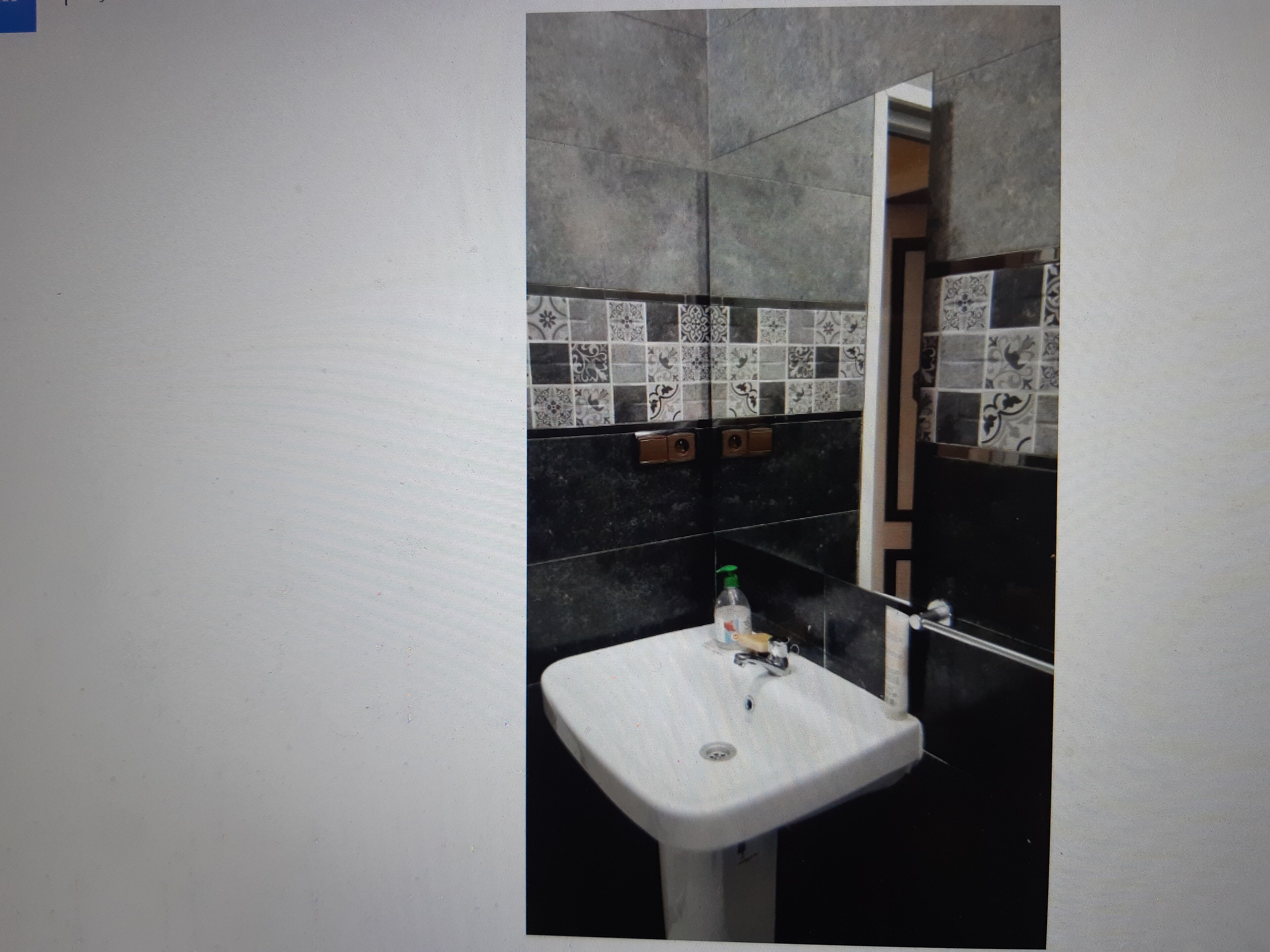 Een badkamer met een witte wastafel, zwart-wit betegelde vloer en een spiegel.