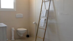 Et moderne badeværelse med glasvægs brusekabine, toilet og en træstige lænet op ad væggen.