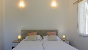 En dobbeltseng med to sengeborde, hver med en lampe, i et rum med en glat væg og et vindue med lette gardiner.