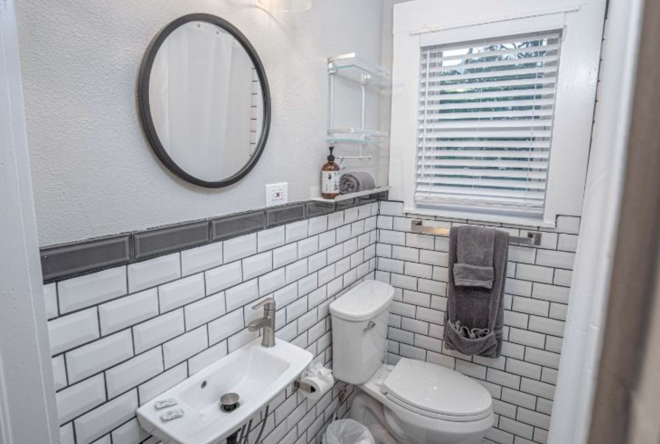 A bathroom with white subway tiles, a white toilet, a white sink, a mirror, and a towel rack.