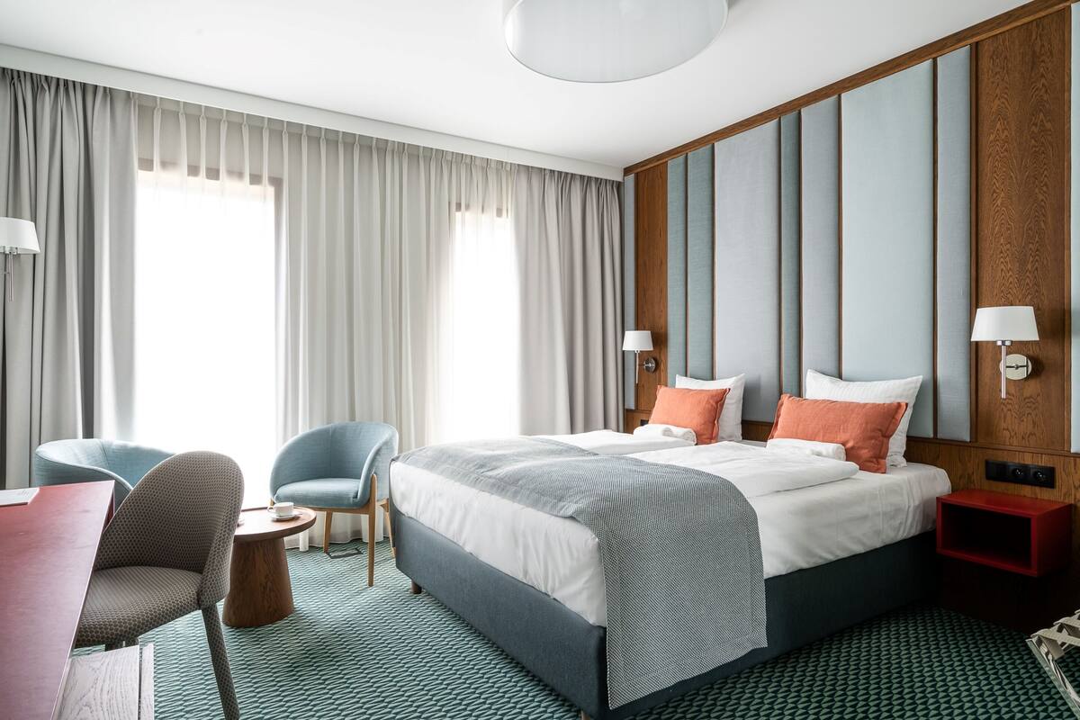 Ein Hotelzimmer mit einem großen Bett, zwei Sessel, einem kleinen Tisch und einem roten Nachttisch.
