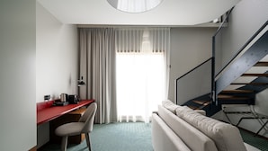 A modern hotel room with a red desk, a beige sofa, a patterned floor, and a staircase with a metal railing. - RentPlanet - Apartamenty Gwarna (Wroclaw)