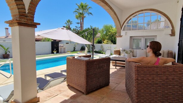 A patio area with wicker furniture, a pool, and a view of palm trees. - Beautiful villa with private pool and garden (Mijas)