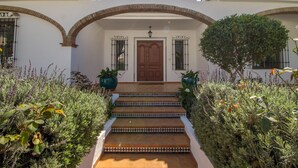 A building with a white facade, a wooden door, and a set of steps leading to the entrance. - Beautiful villa with private pool and garden (Mijas)