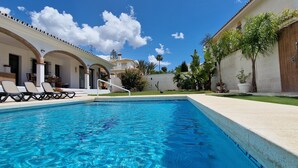 A swimming pool with clear blue water, surrounded by lounge chairs and a building with arches. - Beautiful villa with private pool and garden (Mijas)