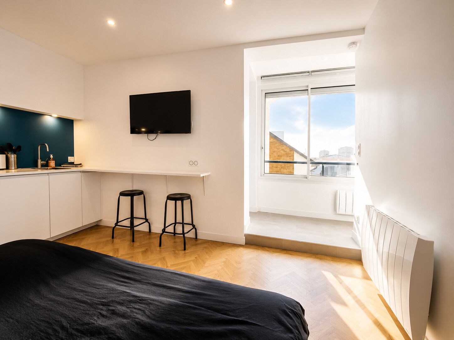 Une chambre moderne équipée d’un lit, d’une télévision, d’une fenêtre donnant sur la ville et d’un coin cuisine.