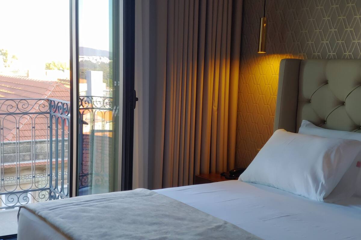 Een hotelkamer met een bed, gordijnen, een muur met een geometrisch patroon en een balkon met een metalen hekwerk.