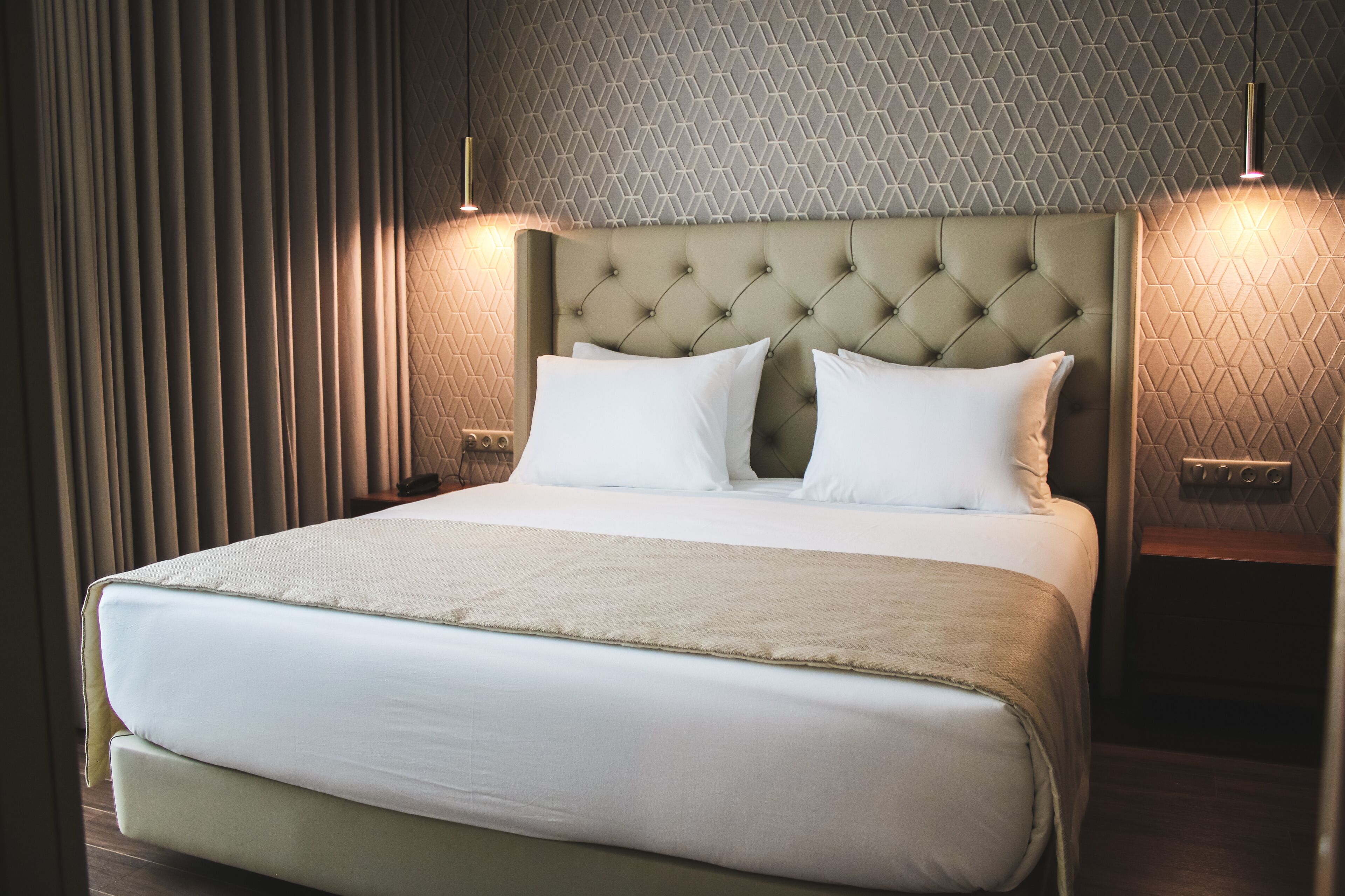 Una habitación de hotel con una cama grande, dos lámparas de noche y un papel tapiz con estampado geométrico.