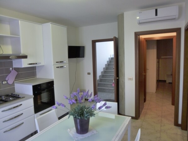 A modern kitchen with white cabinets, a stove, and a dining table with a potted lavender plant.