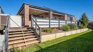 A modern two-story house with a covered patio, a wooden staircase, and a well-maintained lawn.