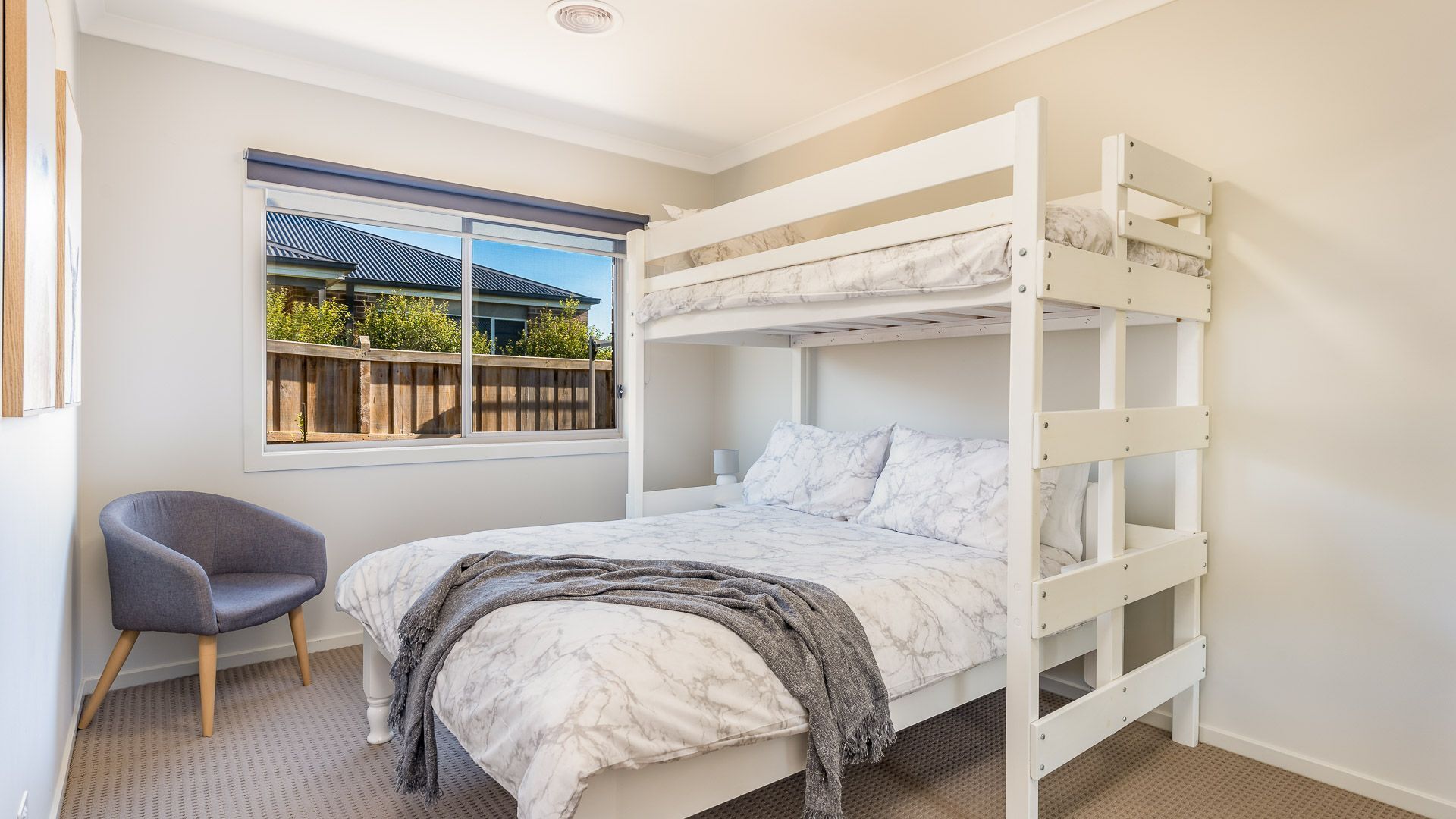 Une chambre avec un lit superposé, une fenêtre, une chaise et une vue sur une maison à l’extérieur.
