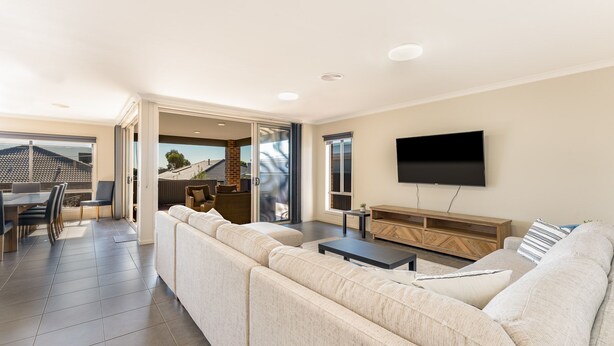 A modern living room with a large sofa, a flat-screen TV, and a dining area with a table and chairs.