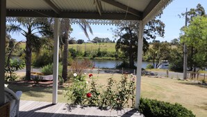 A covered outdoor area with a view of a lake, surrounded by greenery and a parked RV. - Bylands Cottage. Historic home with Tambo River views (Swan Reach)