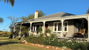A two-story house with a porch, a chimney, and a garden with flowers and shrubs. - Bylands Cottage. Historic home with Tambo River views (Swan Reach)