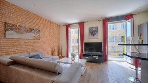 Un saló modern amb paret de maó, un sofà gran, un televisor de pantalla plana i un balcó amb cortines vermelles.