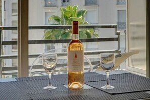 A bottle of Coteaux Varois en Provence wine on a table with two glasses, set on a balcony with a view of buildings and a palm tree. - STUDIO MODERNE LUMINEUX PROCHE CROISETTE A0B132 (Cannes)