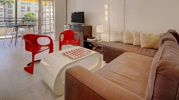A modern living room with a brown sofa, red chairs, a white coffee table, a flat-screen TV, and a lamp.