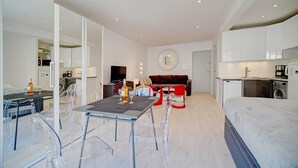 A modern, well-lit room with a dining area, a sofa, and a bed.