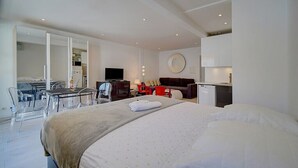 A modern hotel room with a large bed, a desk, a television, and a dining area.