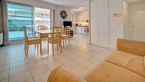A living room with a sofa, a dining table with chairs, a TV, and a kitchen in the background. - 3 PIECES SPACIEUX CANNES CENTRE A2B067 (Cannes)