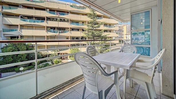 A balcony with a table and chairs, overlooking a multi-story building with balconies. - 3 PIECES SPACIEUX CANNES CENTRE A2B067 (Cannes)