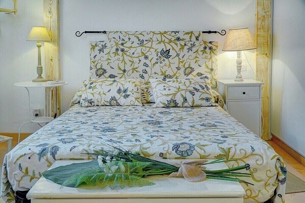 A bedroom with a floral bedspread, bedside lamps, a bedside table, and a bouquet of flowers on the bed.