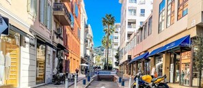 Vista da rua com edifícios, uma motocicleta estacionada e céu claro.
