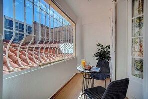 A balcony with a view of terracotta roof tiles, a potted plant, and a table with a chair.