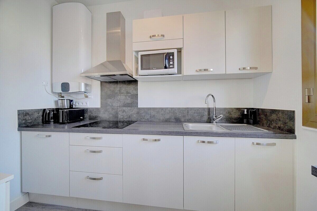 Een moderne keuken met witte kasten, een magnetron, een broodrooster en een spoelbak.